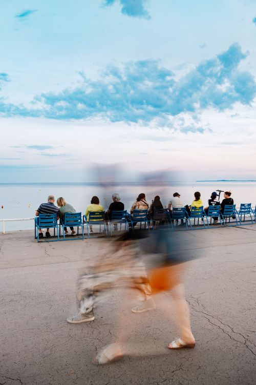 Free Blurred pedestrians and seated viewers enjoying a serene seaside sunset in Nice, France. Stock Photo