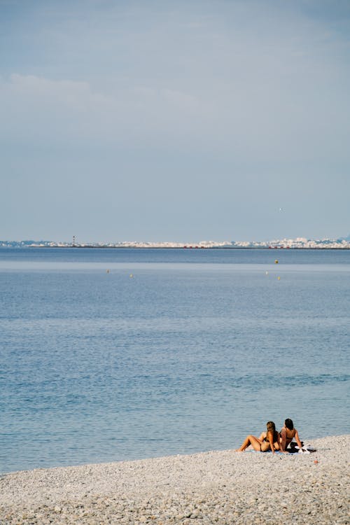 Free Two people sitting on the beach near the water Stock Photo