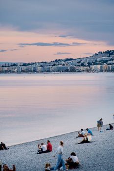 Tranquil beach scene in Nice, France with people relaxing by the sea during a stunning dusk.