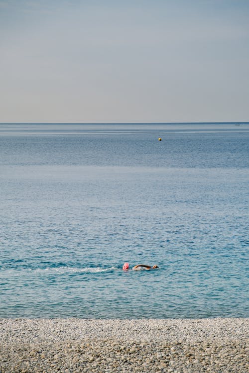 Free A person swimming in the ocean near a beach Stock Photo