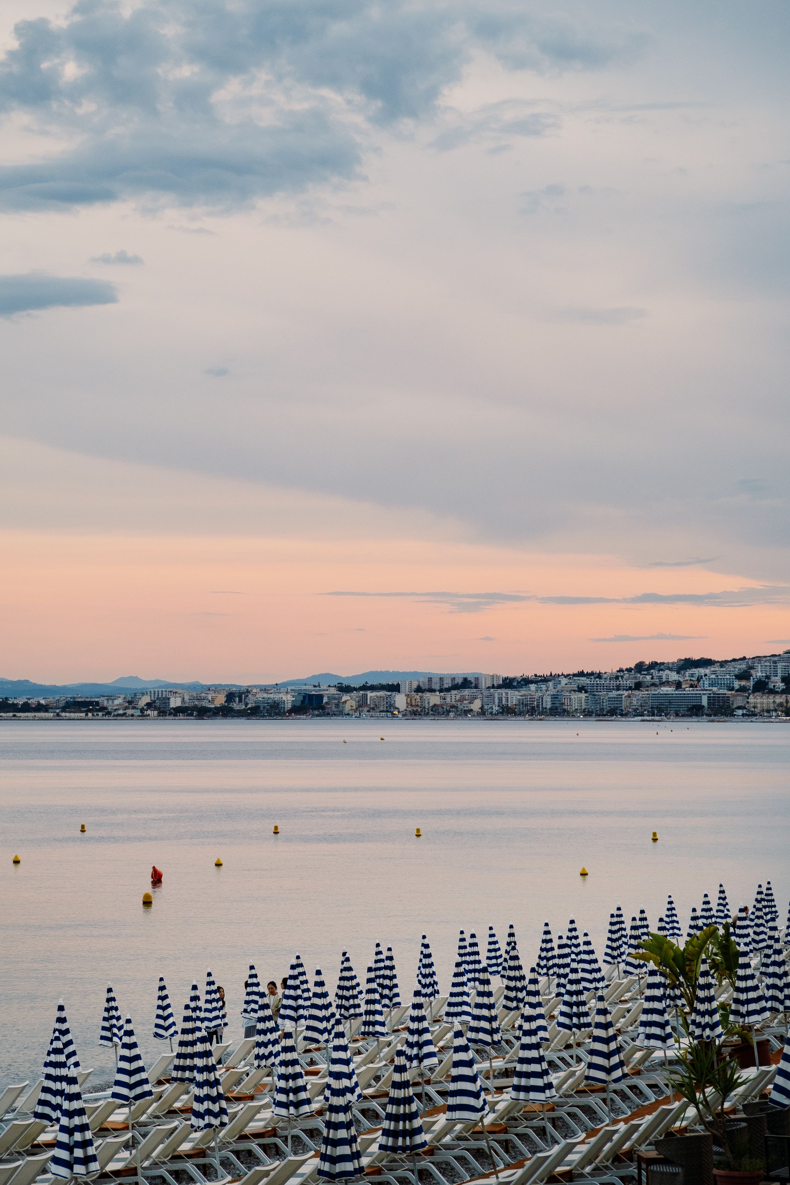 Serene evening view of Nice beach with striped umbrellas at sunset.