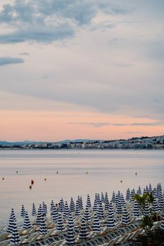 Serene evening view of Nice beach with striped umbrellas at sunset.