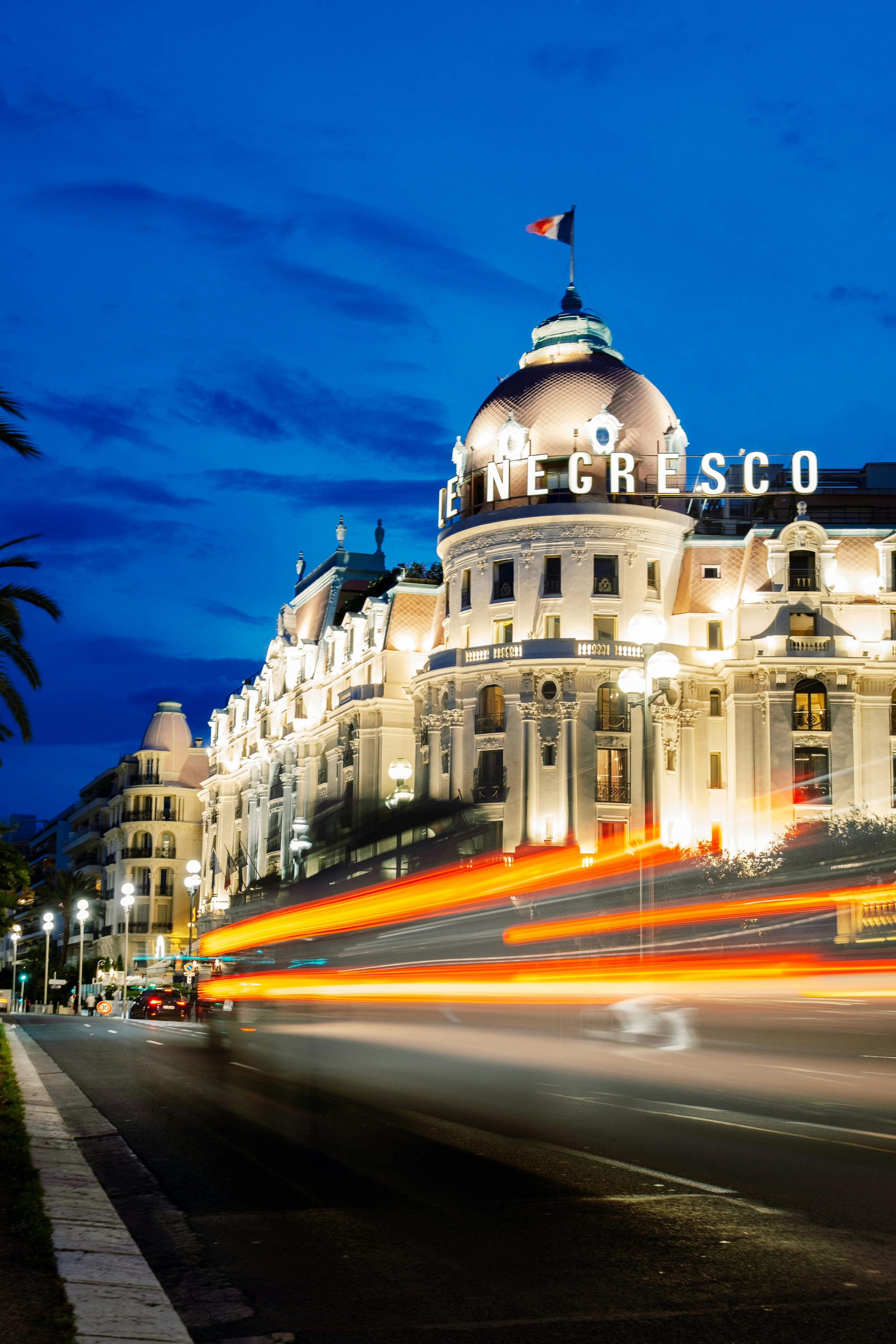 Illuminated Le Negresco Hotel in Nice with vibrant light trails during night time.
