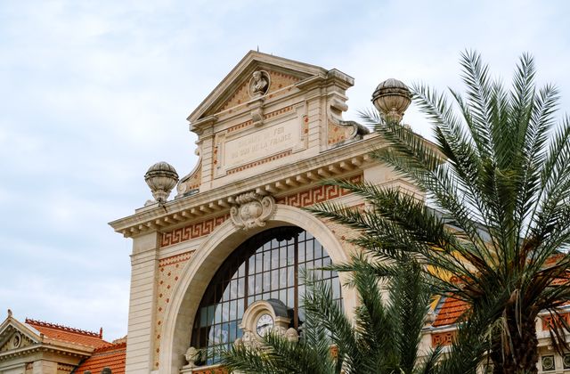 Classic French architecture with palm trees under a clear sky, highlighting intricate design and elegance. — arriving in Nice, Alpes-Maritimes
