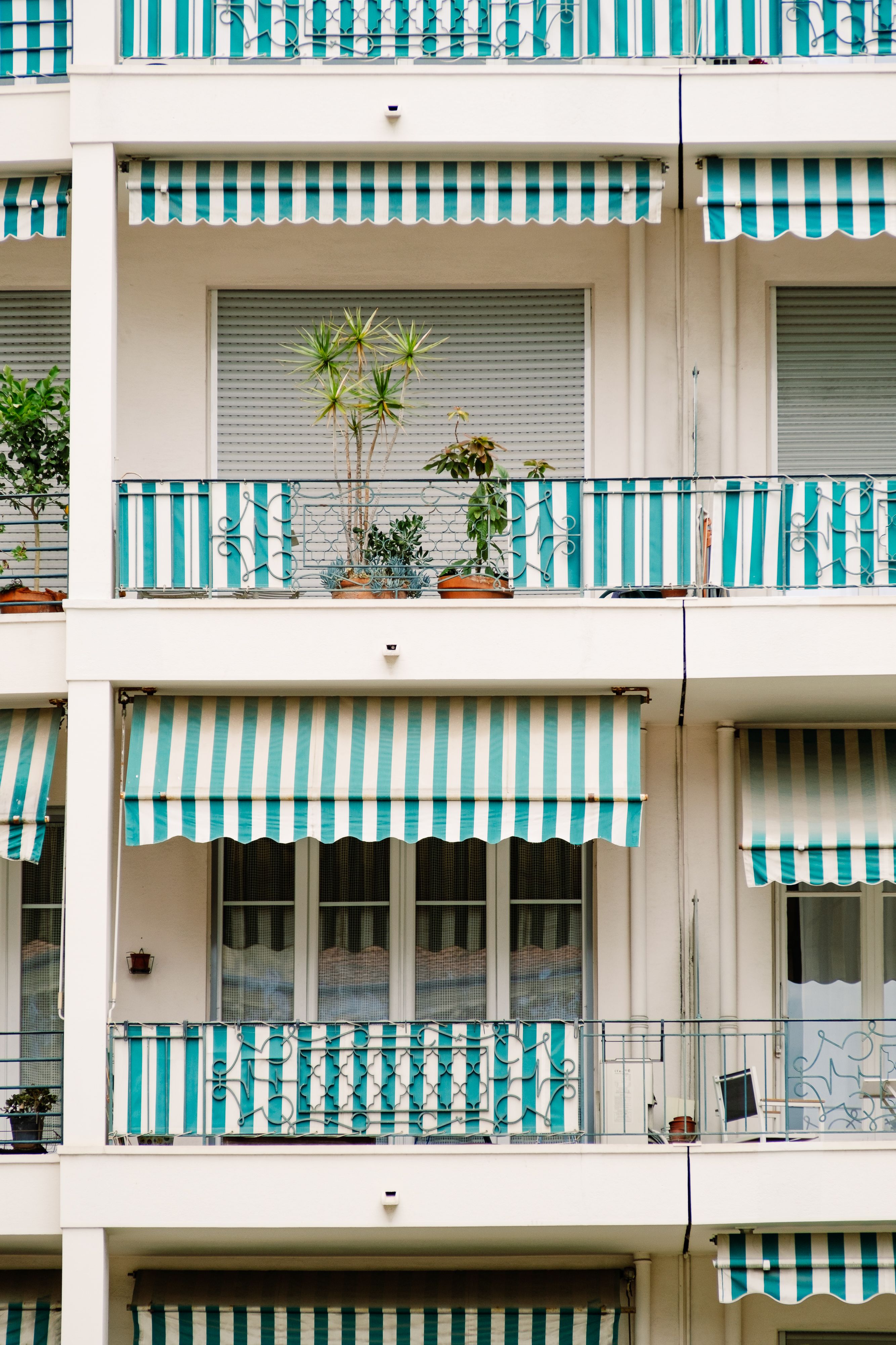 Contemporary urban apartment building featuring green-striped awnings and potted plants on balconies.