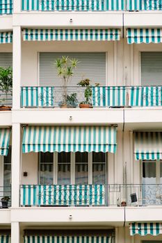 Contemporary urban apartment building featuring green-striped awnings and potted plants on balconies.