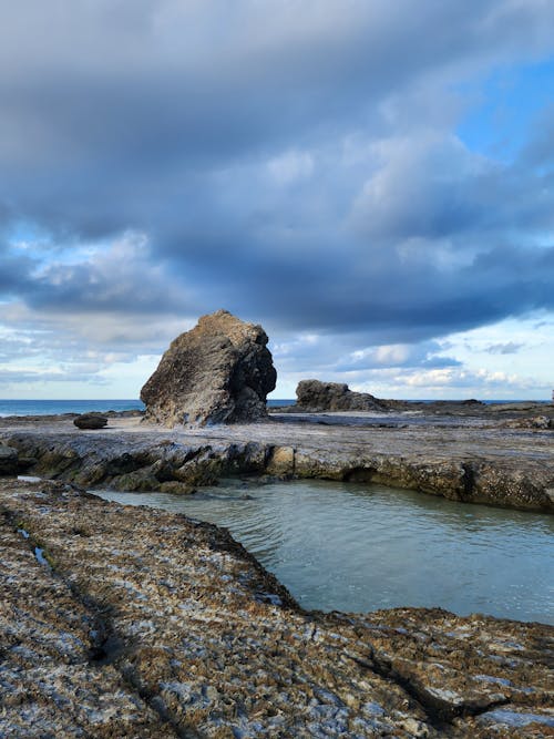 A rock formation in the ocean with a cloudy sky