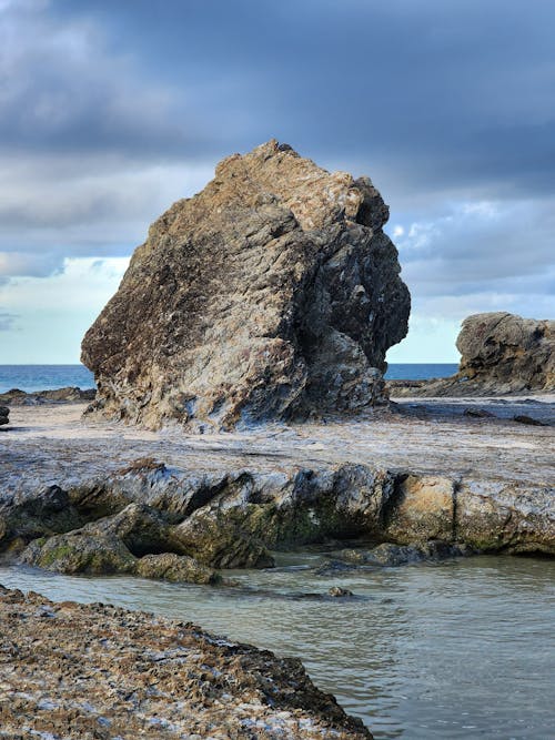 A large rock sitting on the beach near the water