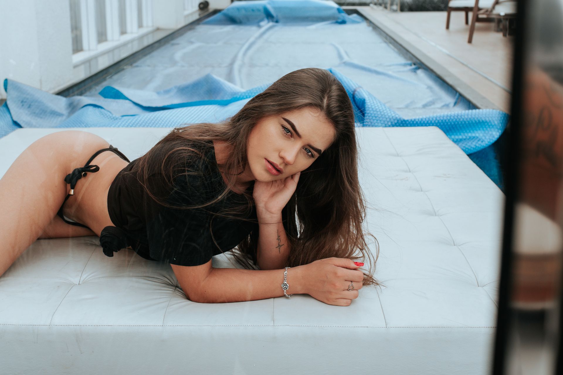 Photo of Woman in Black T-shirt and Bikini Bottoms Lying on White Leather Poolside Sofa