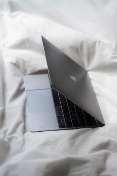 A luxury laptop sits elegantly on soft white sheets, highlighting its minimalist design.