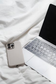 Minimalist photo of a smartphone and laptop on white sheets, showcasing modern technology.