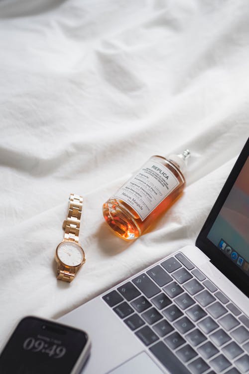 A laptop, a bottle of perfume and a watch on a bed