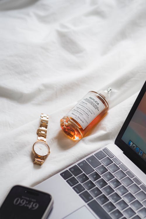 Free A laptop, a bottle of perfume and a watch on a bed Stock Photo