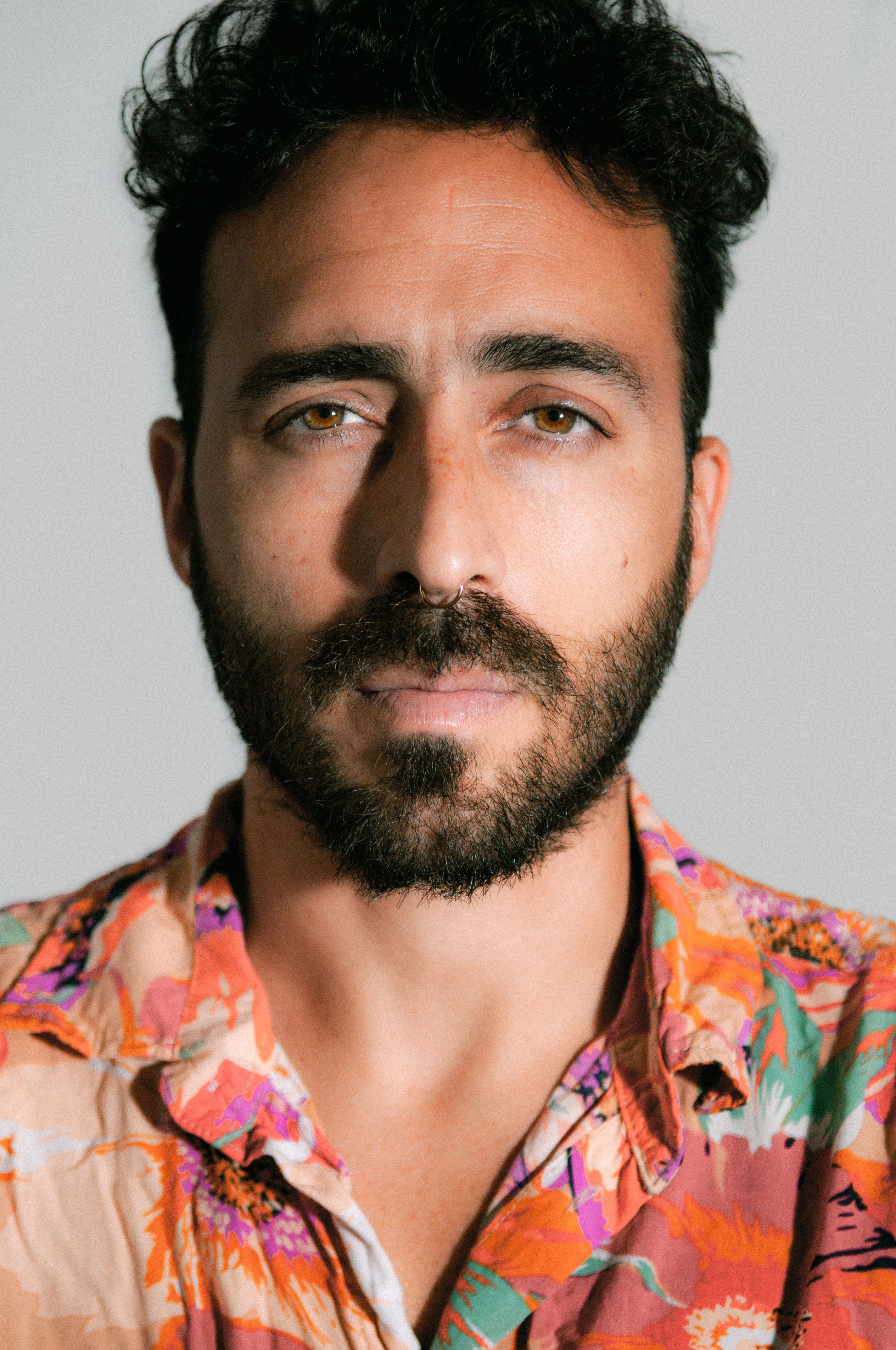 Close-up portrait of a man with a beard and colorful shirt in studio lighting.