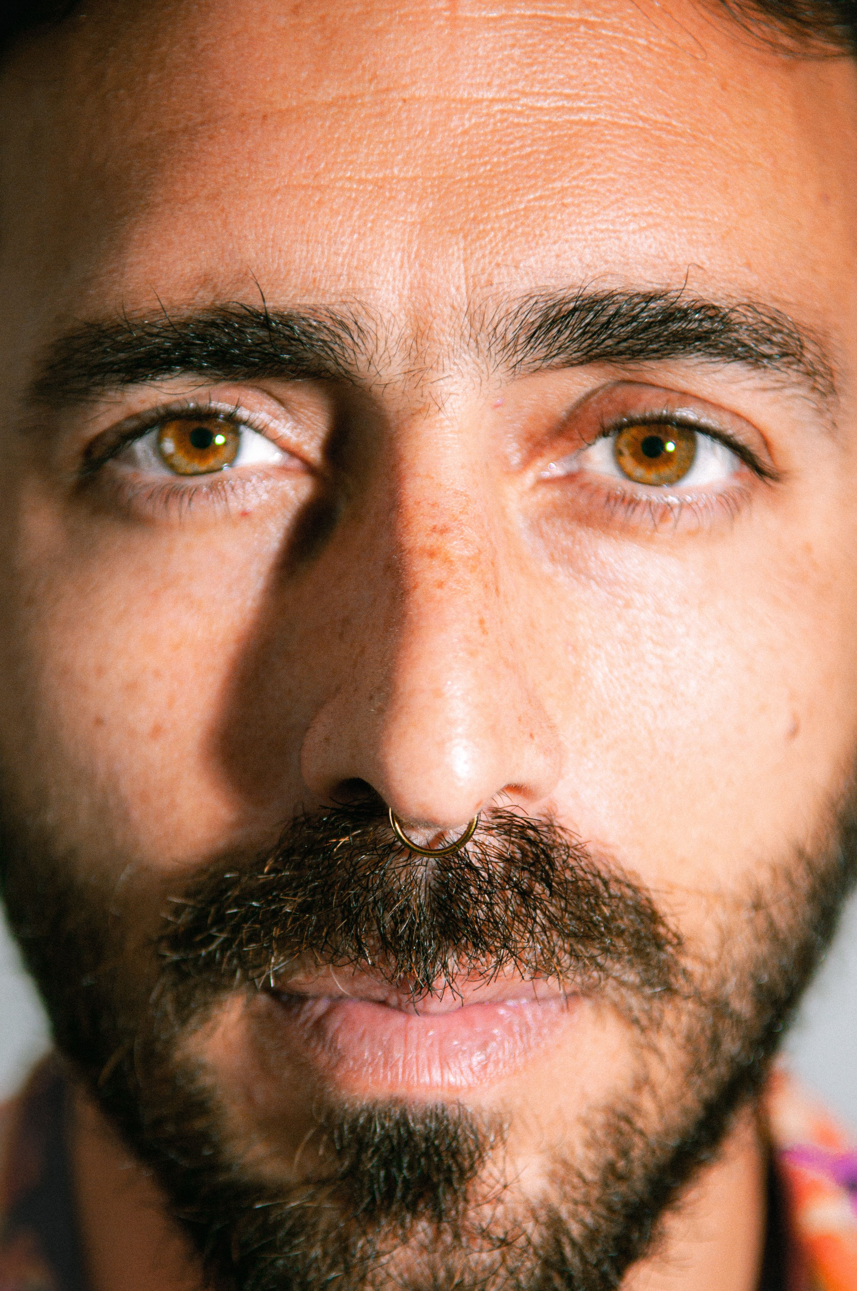 Intense close-up portrait of a man with a beard and brown eyes, highlighting facial features.