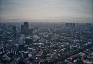 从空中俯瞰雅加达的现代天际线，烟雾弥漫在城市景观之上，展现出密集的城市建筑