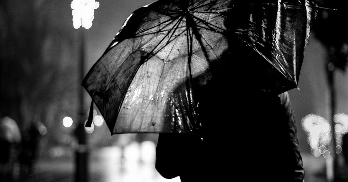 Grayscale Photography of Person Holding Umbrella Beside Post