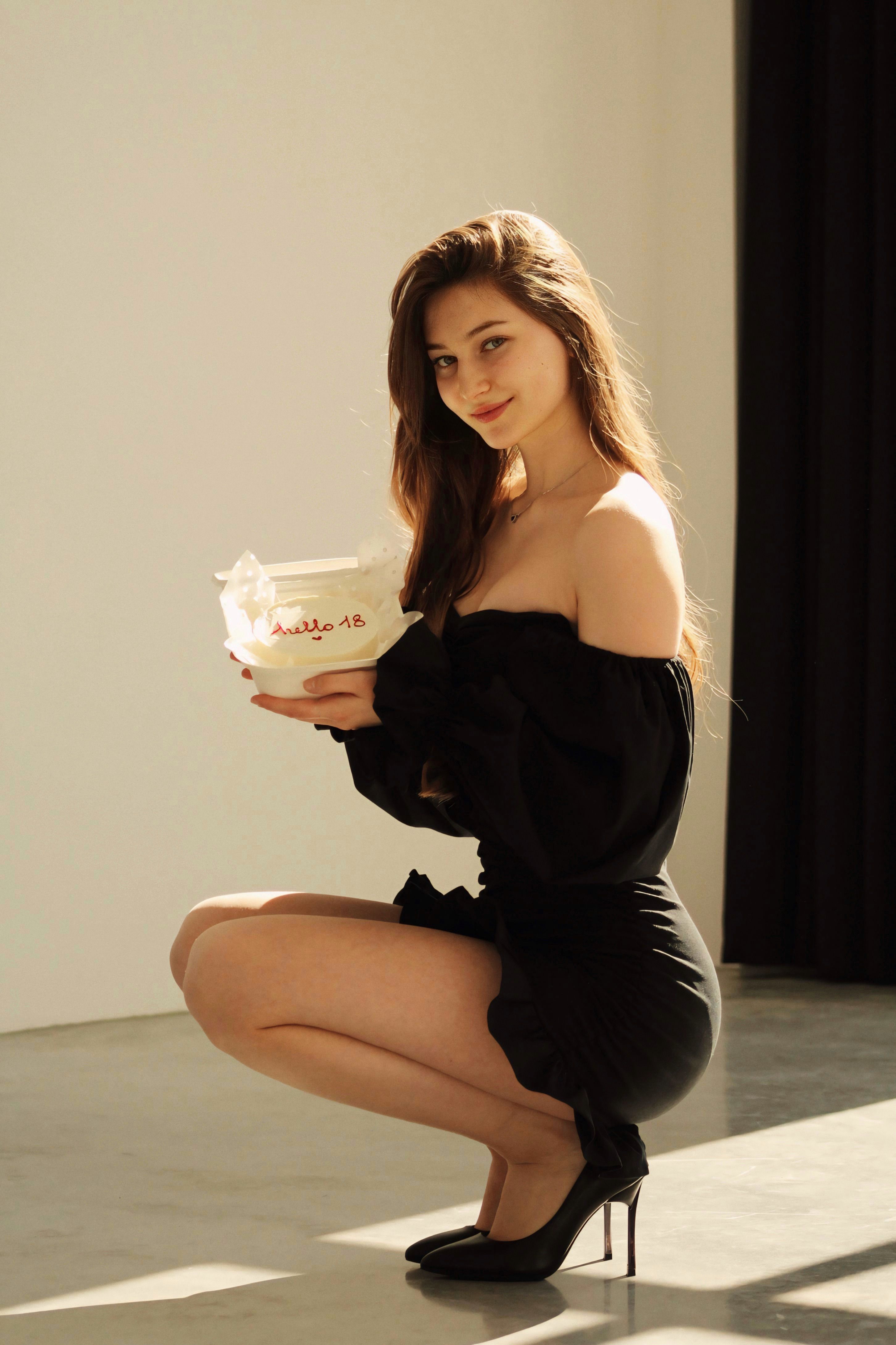 Young woman in black dress holding a birthday cake, embodying elegance and celebration.