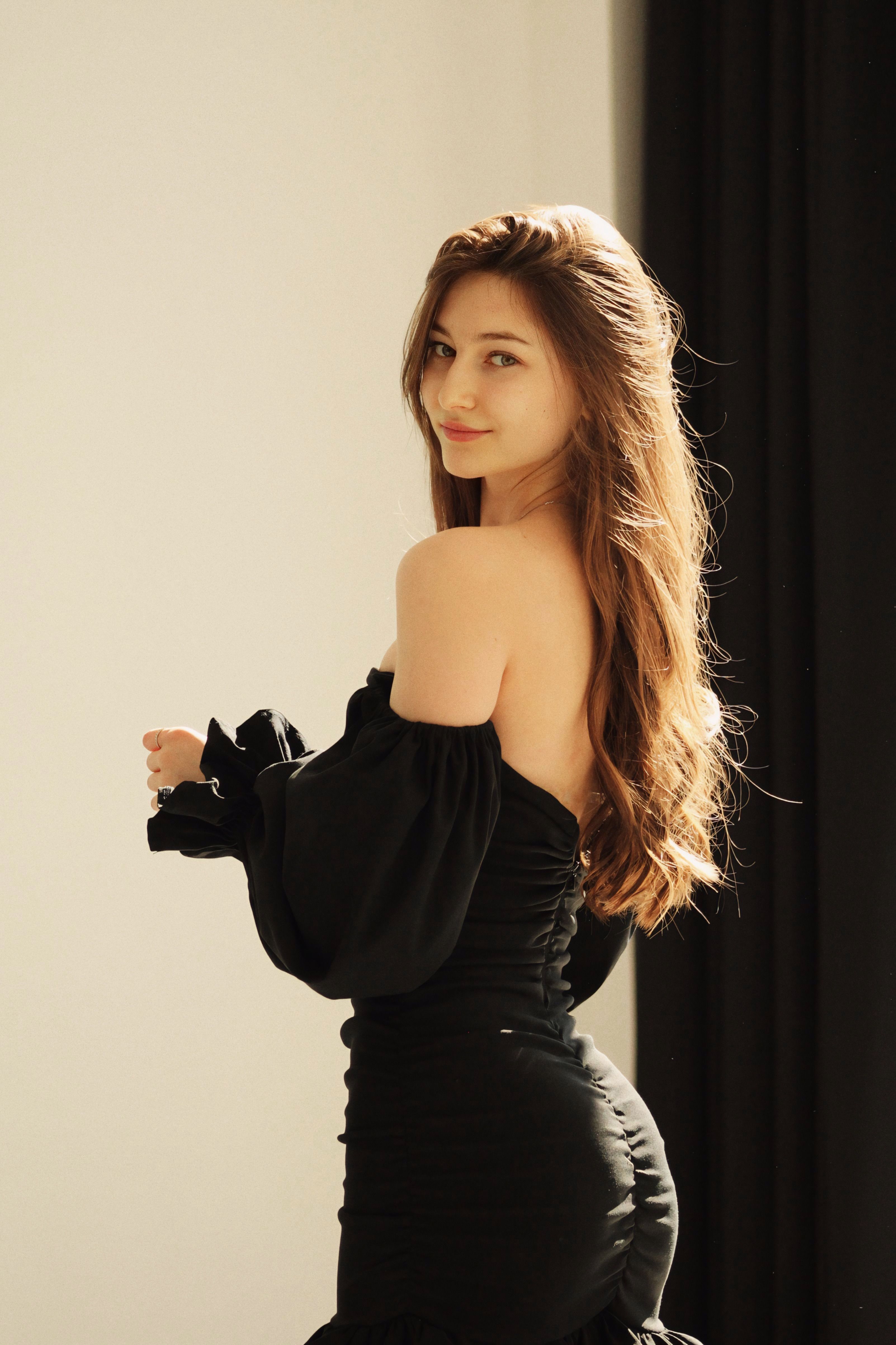 Elegant woman in a black off-shoulder dress posing gracefully indoors with soft lighting.