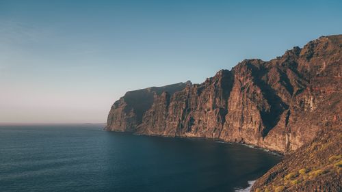 Free Breathtaking view of a rugged cliff meeting the serene ocean under a clear sky. Stock Photo