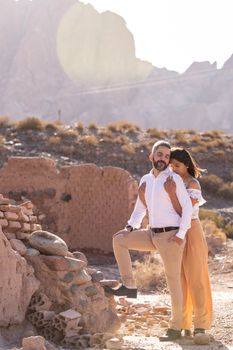 Romantic couple sharing an affectionate moment in a sunlit desert landscape with ancient ruins.