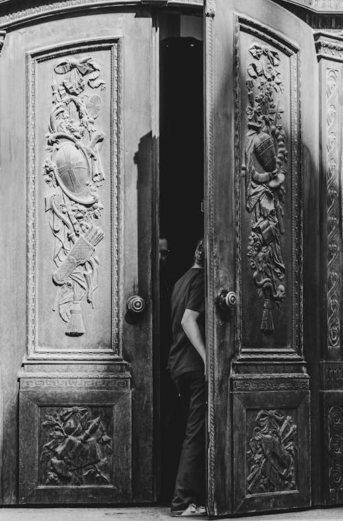 A black and white photo of a man standing in front of a door