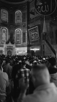 A black and white photo of a crowded mosque interior during prayer.