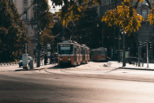 A classic tram navigates through Budapest's urban streets on an autumn day, with sunlight highlighting the scene.