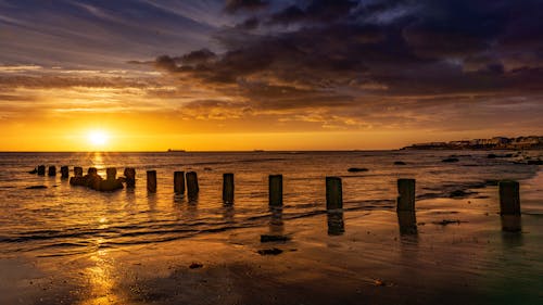 A sunset over the ocean with wooden posts