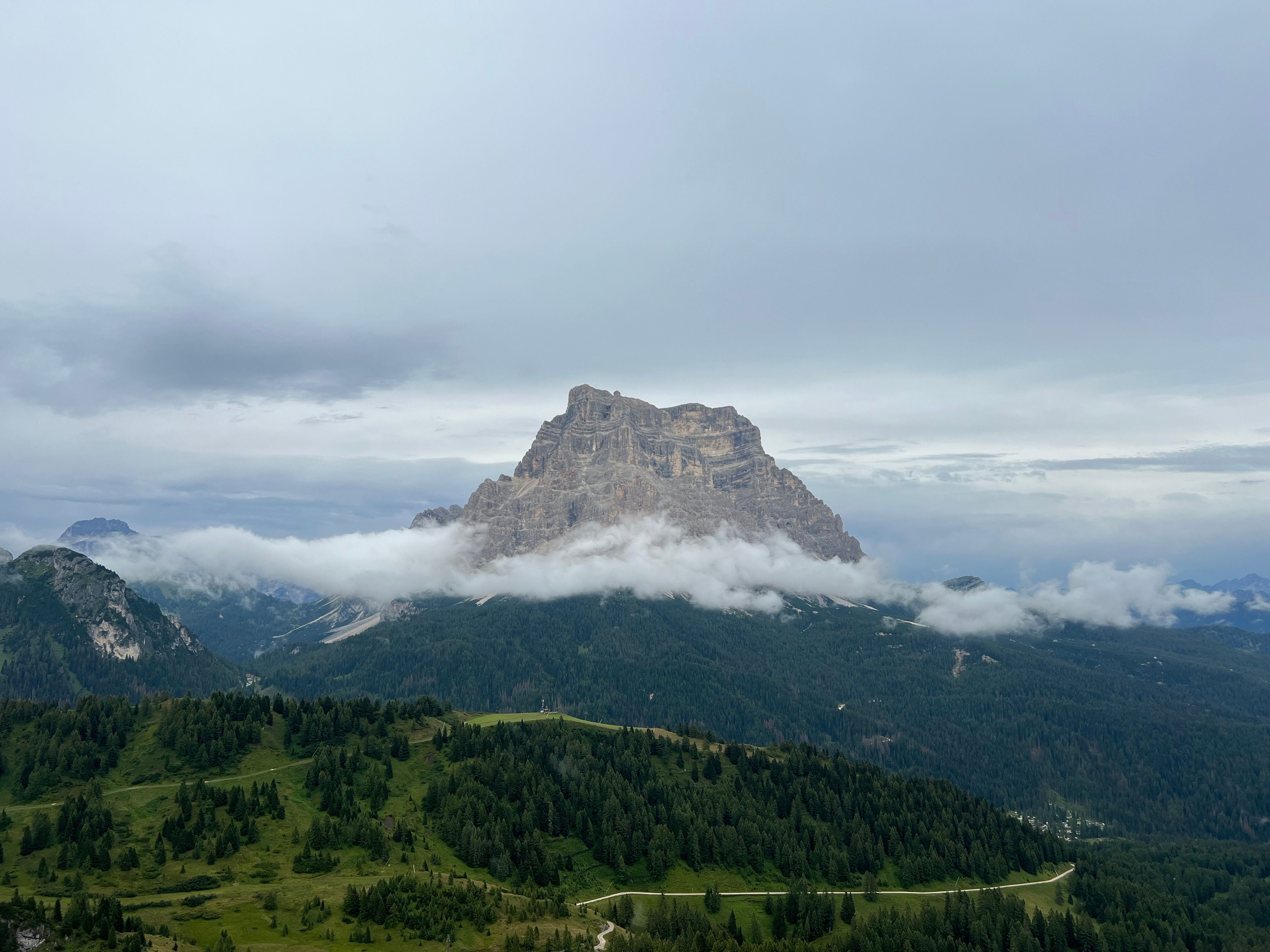Breathtaking view of Monte Pelmo in the Dolomites with lush forests and misty clouds.