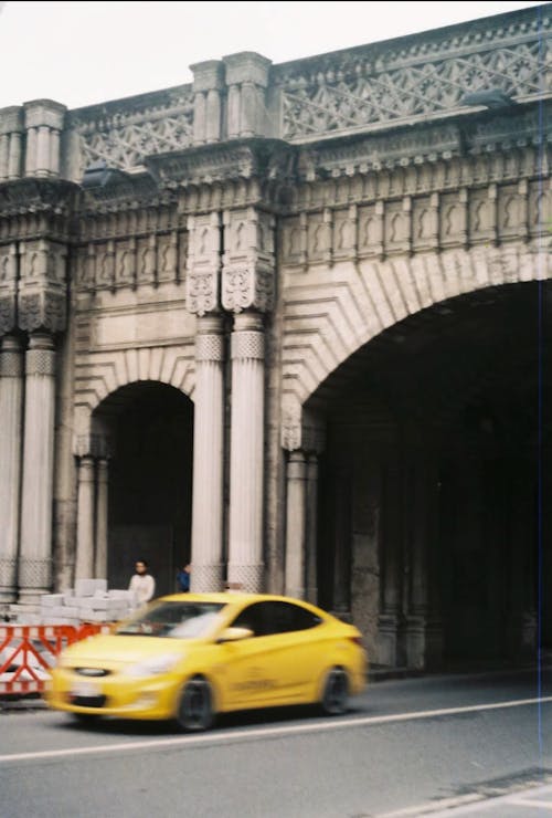 A yellow taxi drives under a bridge