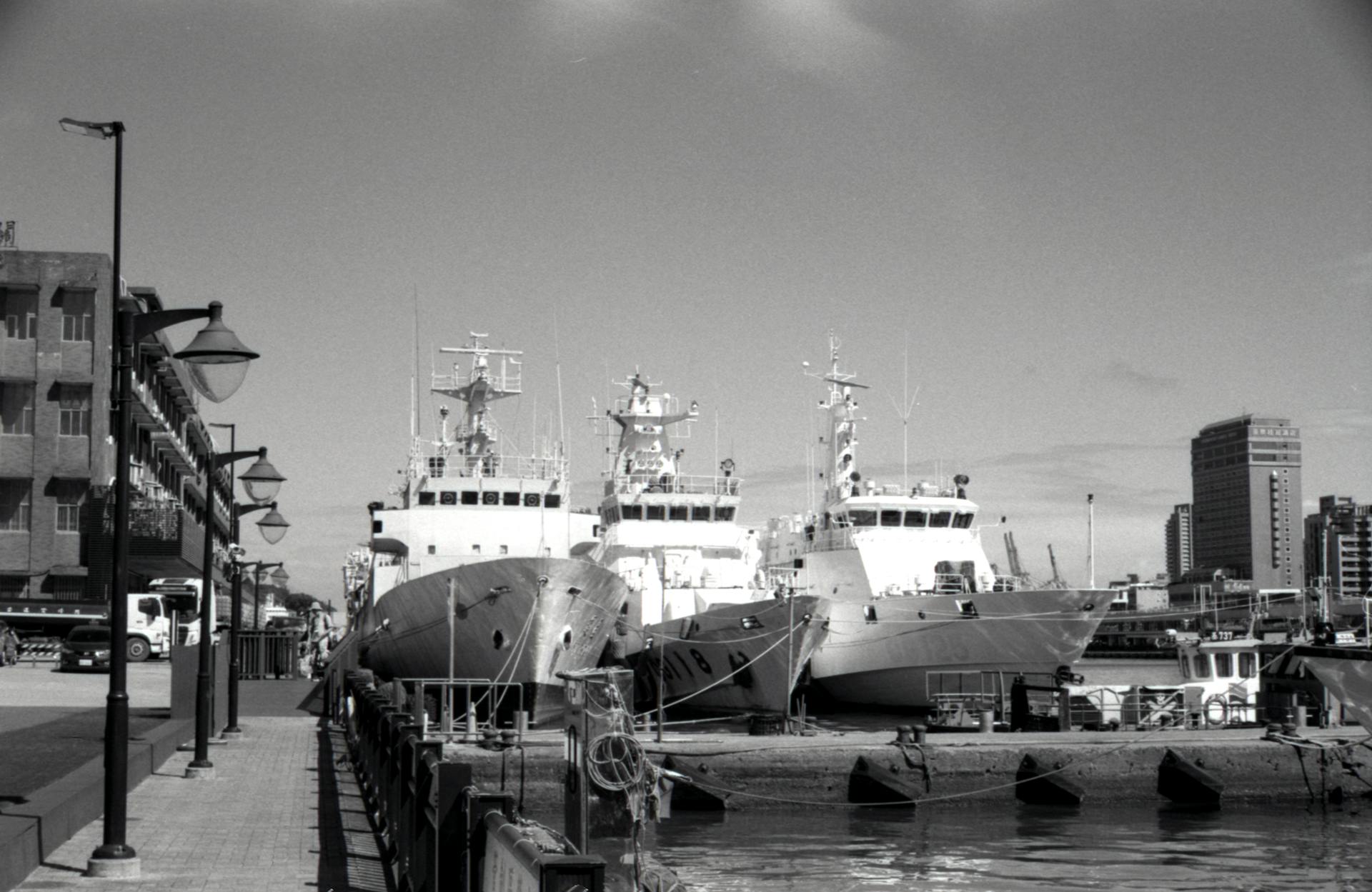 Monochrome view of naval ships docked at Taipei harbor with city backdrop.