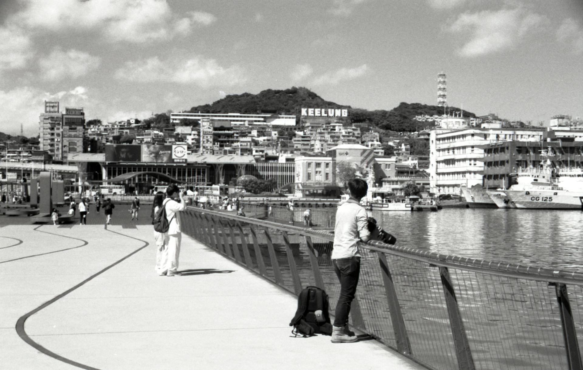 Scenic black and white view of Keelung City waterfront in Taiwan with people and buildings.