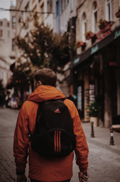 Uomo In Giacca Arancione Con Zaino Adidas Nero Cammina In Mezzo Alla Strada