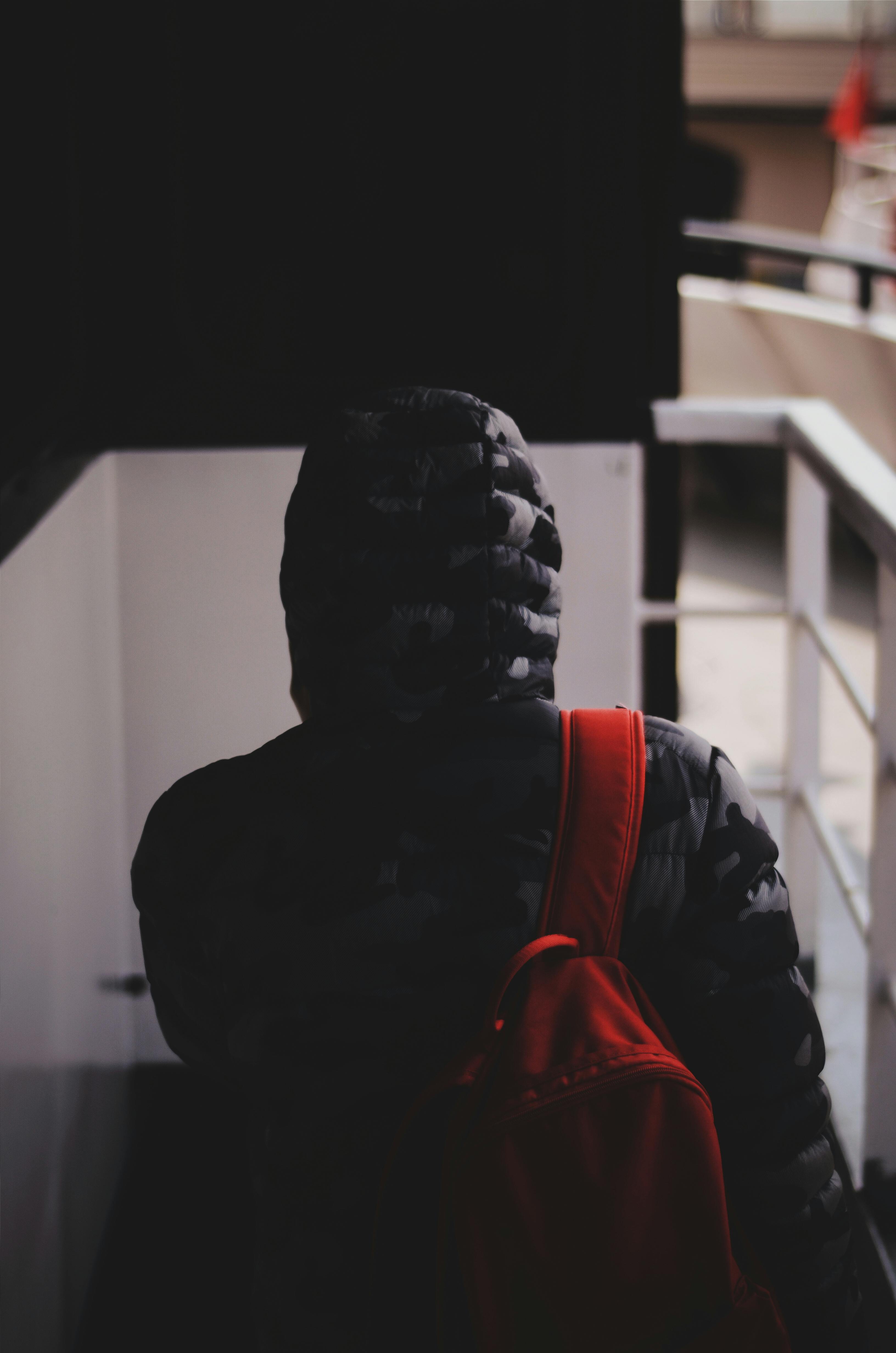 从后面看去，一个穿连帽衫的人背着红色背包，正在室内行走