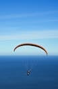 在晴朗的蓝天下，一个人用橙色降落伞在广阔的海洋上滑翔