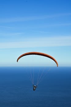在晴朗的蓝天下，一个人用橙色降落伞在广阔的海洋上滑翔