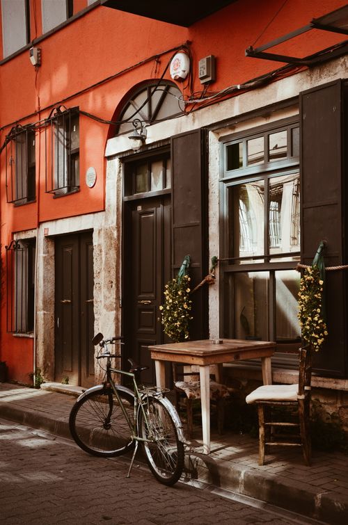 Free A picturesque street view featuring a bicycle and an inviting cafe setup against a vibrant building facade. Stock Photo