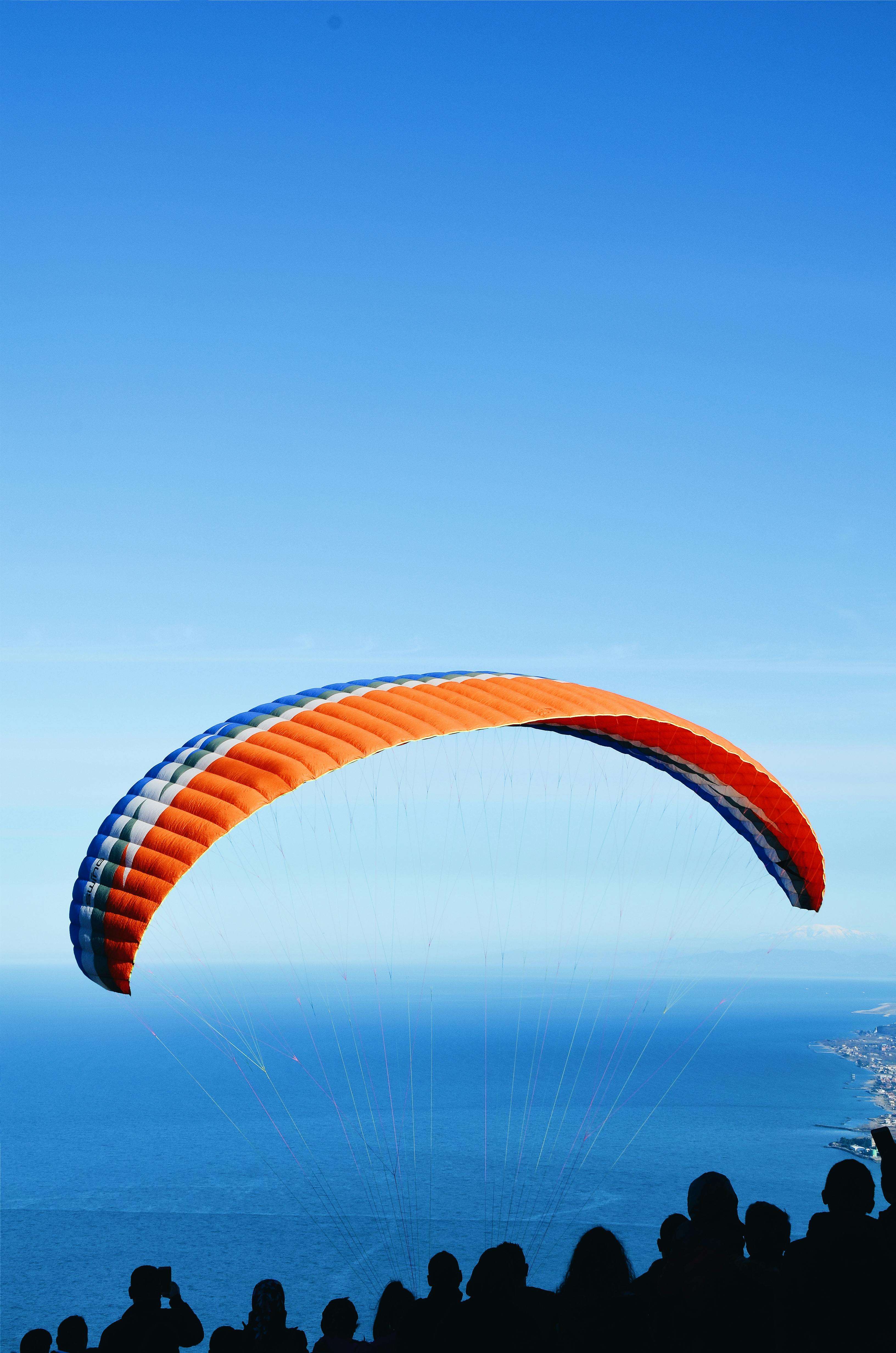 人们看着滑翔伞在海洋上空翱翔的剪影，捕捉旅行的兴奋与空中冒险