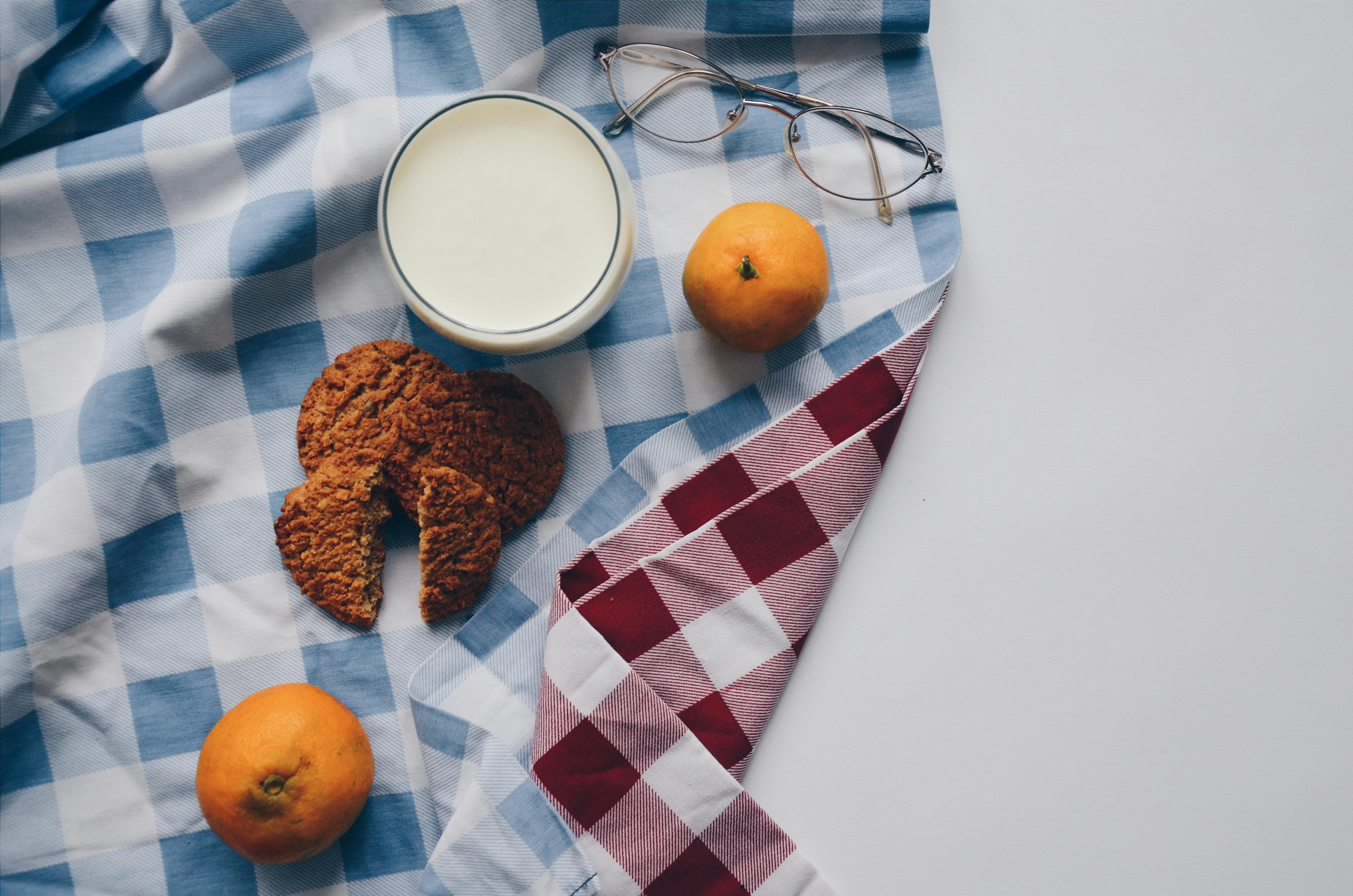 two oranges two cookies and a cup of milk on table