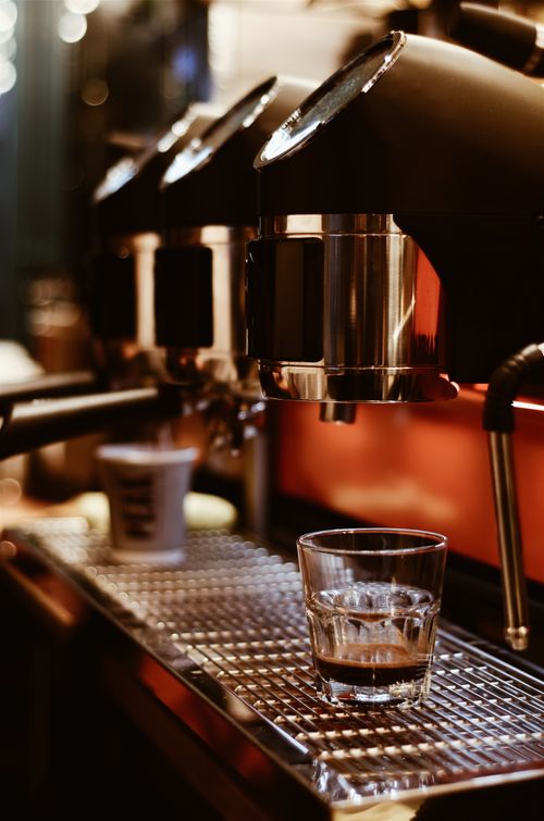 Free A fresh shot of espresso pours into a glass from a sleek coffee machine in a cozy cafe. Stock Photo