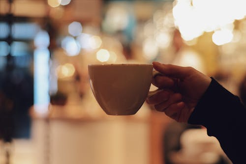 Shallow Focus Photo of Hand Holding White Ceramic Mug