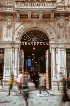 Blurred pedestrians passing by the historic Grand Pera building entrance.