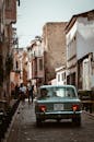 一辆经典汽车行驶在一条历史悠久的街道上，两旁是乡村建筑和行人