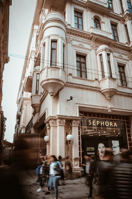 Blurry pedestrians walking past a vintage building with ornate details and shopfront in an urban area.