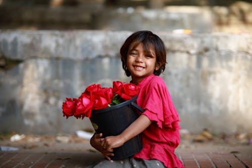 A little girl holding a flower pot with red roses