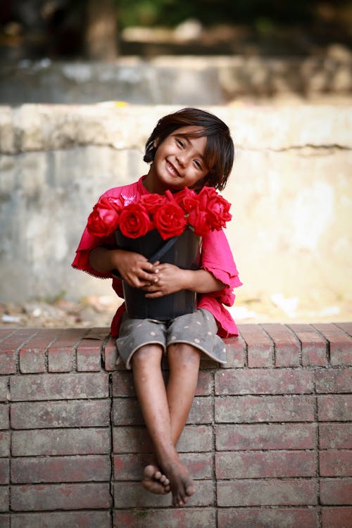 A little girl sitting on a brick wall holding a bunch of roses
