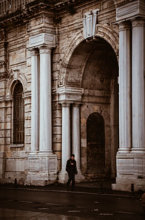 Free A lone person walks by grand architectural arches and columns, evoking historical grandeur. Stock Photo