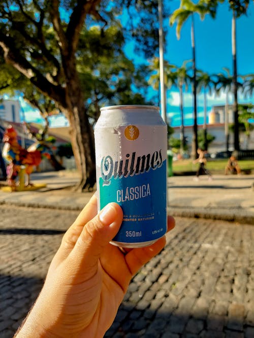 A hand holding a can of beer in front of a street