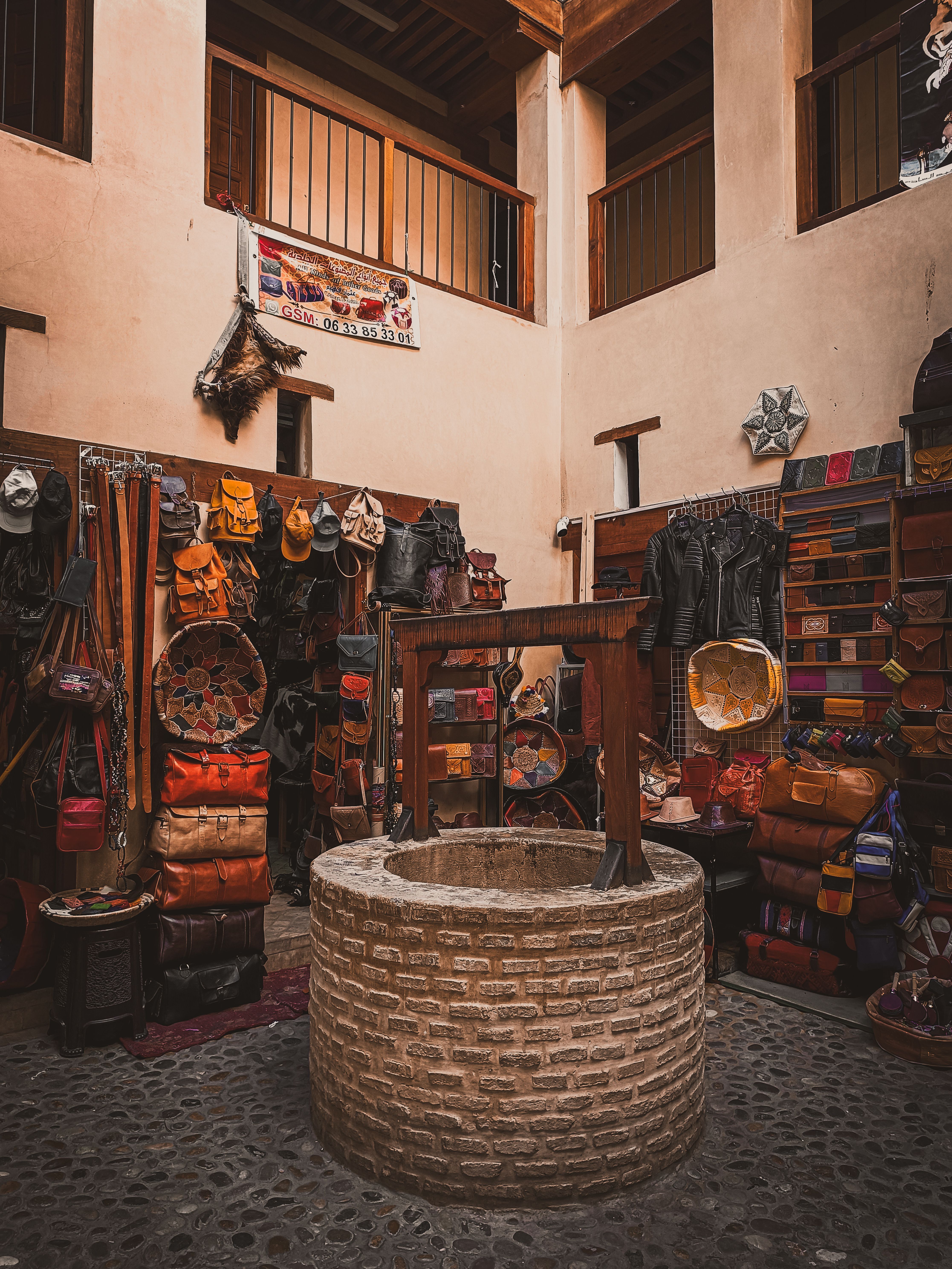 Explore a cozy traditional shop with a stone well, surrounded by vibrant leather goods and textiles.